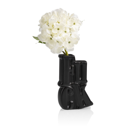 Fuck vase in black with a bunch of white flowers arranged in the letter-shaped neck.