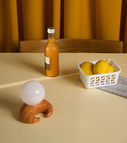 Croissant lamp with a glowing white sphere on a table next to a bottle and lemons