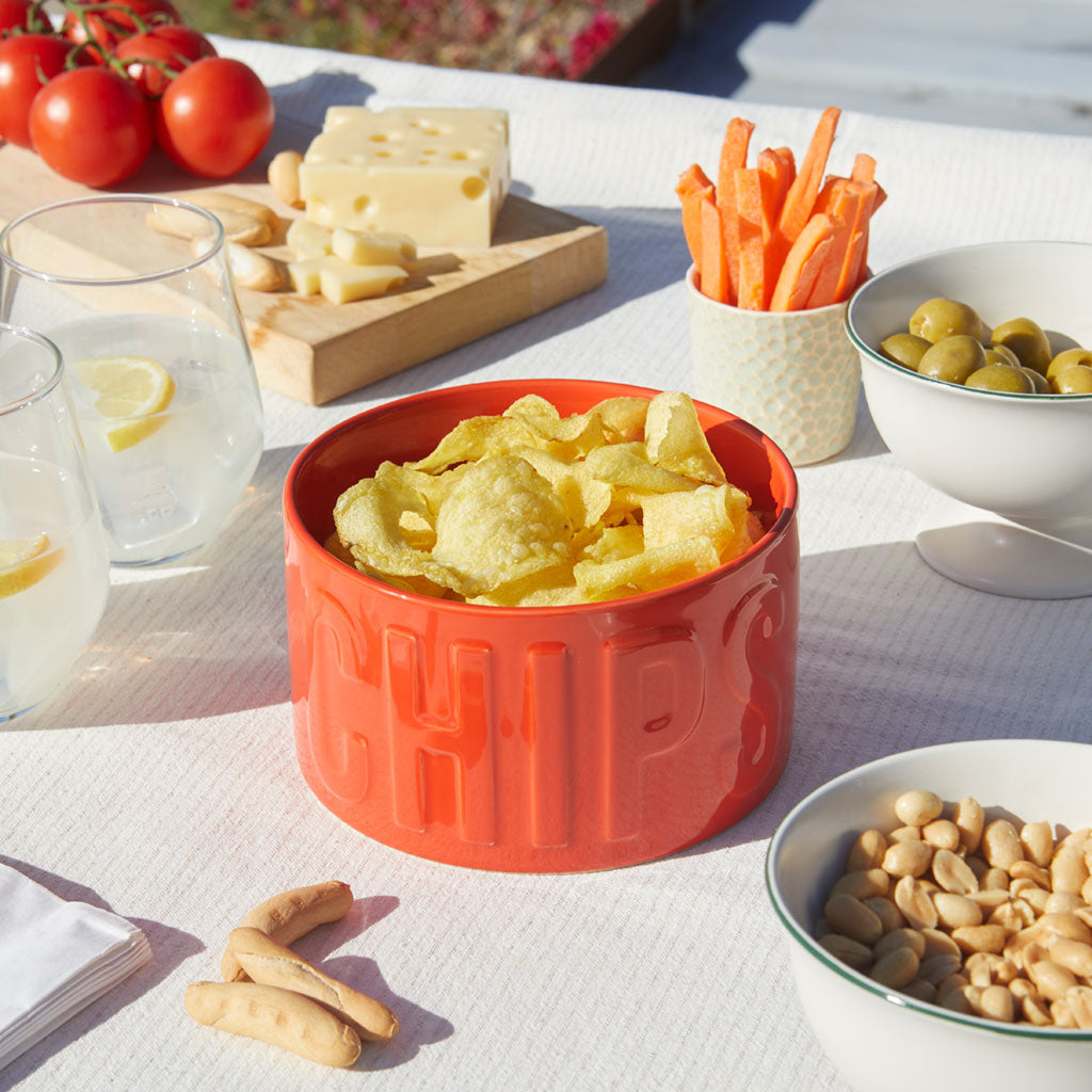 Ciotola Snack Chips rossa su una tavola apparecchiata con pomodori, formaggio, carote e olive