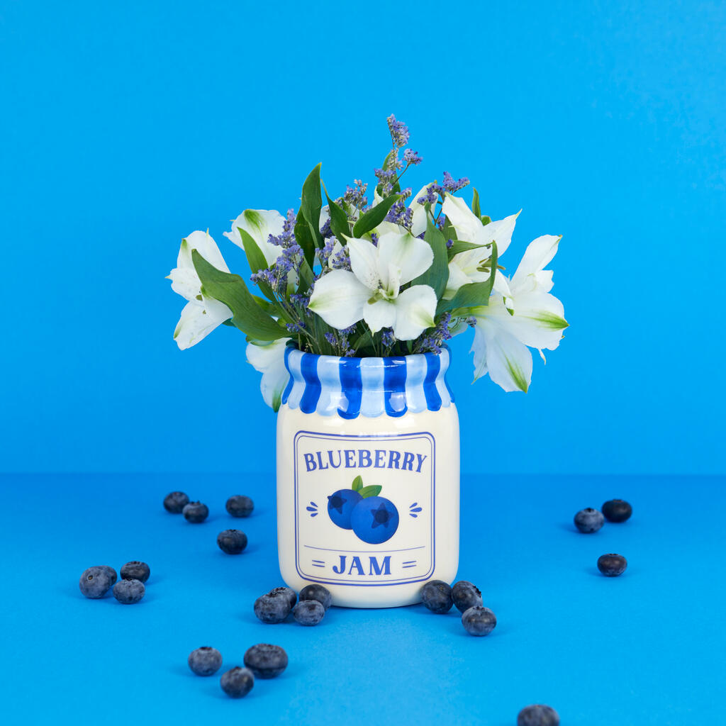 Jam vase, blueberry version with flowers, surrounded by loose blueberries on blue