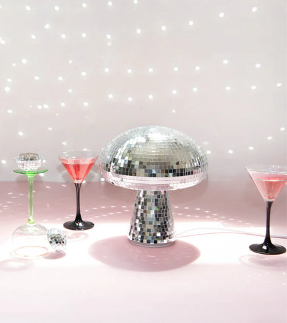 Disco mushroom lamp lit among cocktail glasses against a pink backdrop