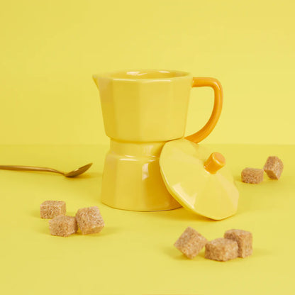 Yellow Moka Cup on a yellow background, lid removed, with brown sugar cubes