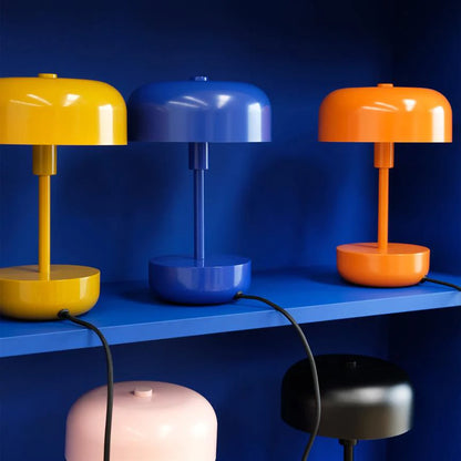 Three Haipot lamps in yellow, blue and orange, lit on a blue shelf, with two more below.