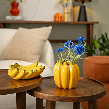 Bananas vase in yellow shaped like a bunch, styled with blue cornflowers, next to a decorative bunch.
