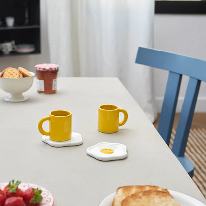 Sunny Side Up coffee cup set yellow mugs on egg-shaped saucers, set on a breakfast table.