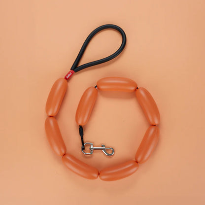 Hot Dog dog leash made of connected orange sausage shapes, laid flat on an orange background.
