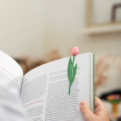 Tulip Bookmark pink tulip bookmark slipped between the pages of an open book, held by a hand.