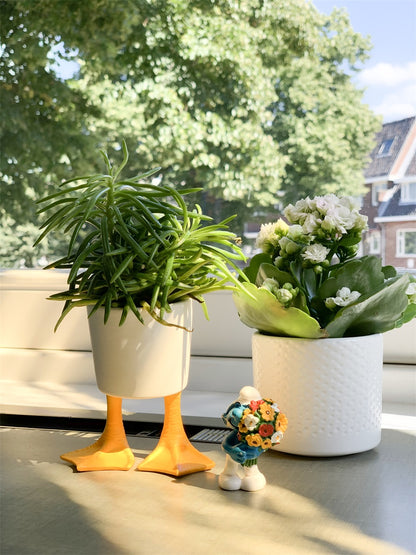 Two Duck Feet planters with green plants on a windowsill, next to a small figurine.