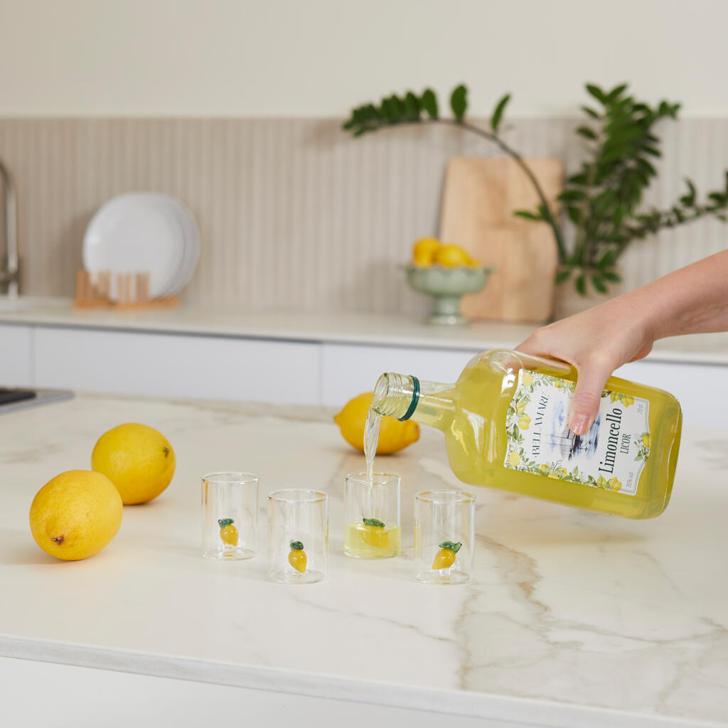 Lemon Shot Glass Set: a hand pouring the yellow liqueur from the bottle into the glasses.