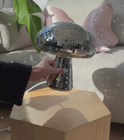 Disco mushroom lamp resting on a stool with a hand touching it