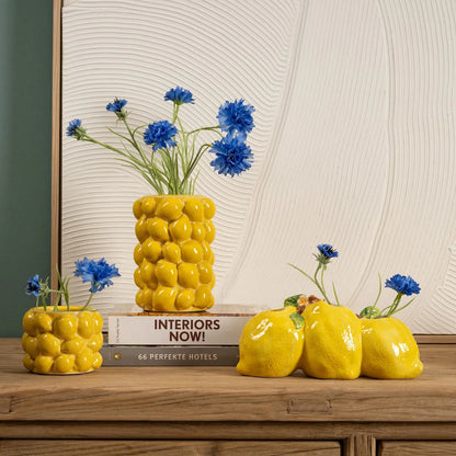 Zest vase in yellow with a rounded bunched shape, styled with blue cornflowers, next to a lemon-shaped vase.