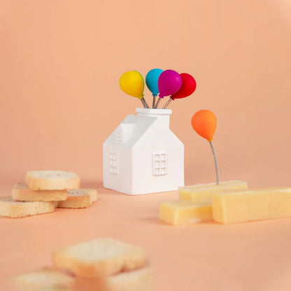 Balloon-shaped cocktail forks with the house holder, among bread slices and cheese, on an orange background.
