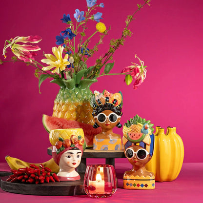 Bananas vase in yellow shaped like a bunch, in a tropical scene with head-shaped pots and a pineapple vase.