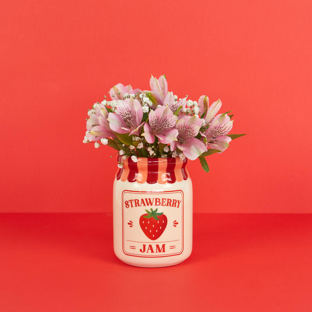 Jam vase, strawberry version with pink flowers, shot straight on against a red background
