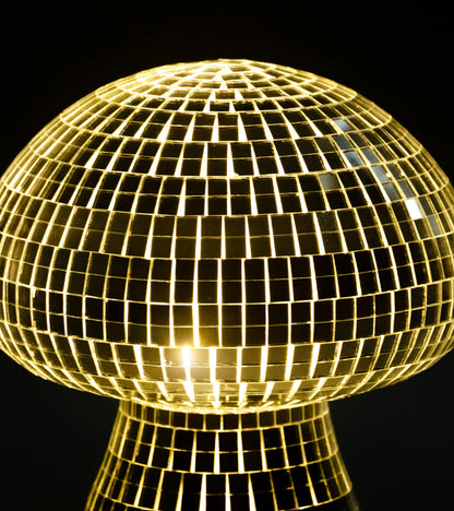 Mini disco mushroom lamp lit beside pink flowers on a light backdrop