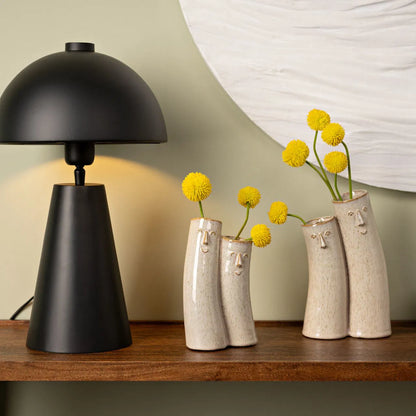 Couple vase in beige shaped like two faces, styled with yellow pom-pom flowers on a shelf.