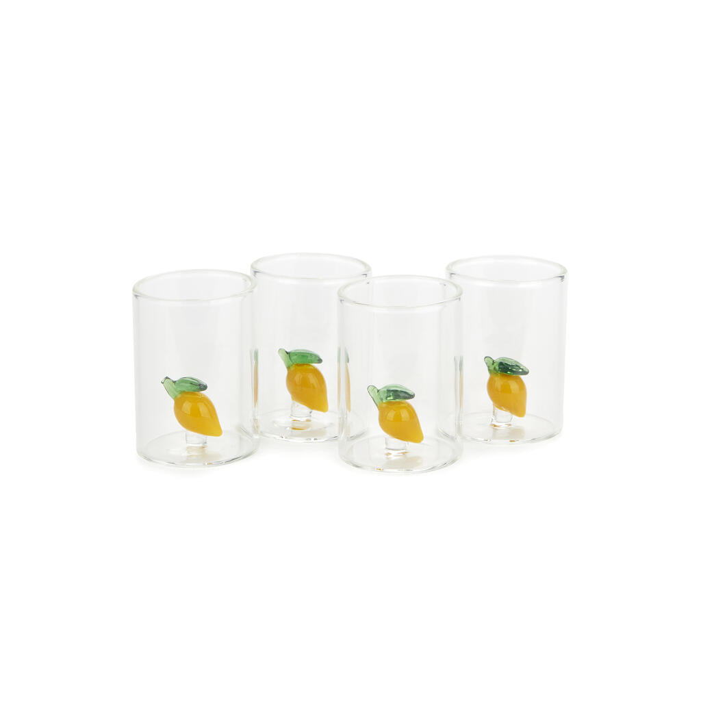 Four small clear glasses each with a decorative lemon inside, on white