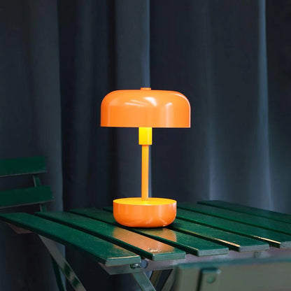 Haipot rechargeable lamp in orange, lit on a green outdoor table at dusk.