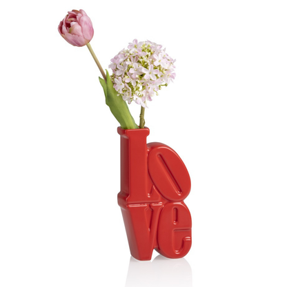 Love vase in red, shaped like lettering, styled with a pink tulip and white flowers, front view.