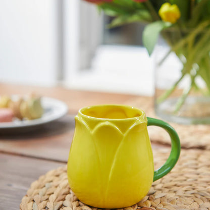 Yellow Tulip mug on a table with a vase of flowers in the background