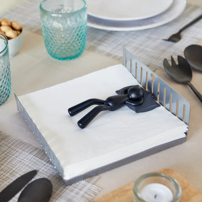 Nap napkin holder in grey, with the sleeping figurine resting on the napkins, set on a table.