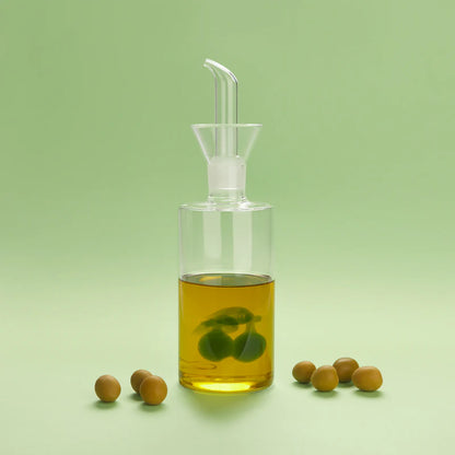 Olive oil cruet filled with oil, with real olives scattered around, green background