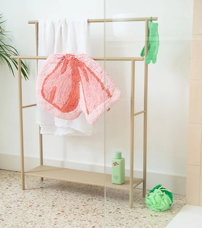Soft bow rug in pink lying on the floor next to a towel rack in a bathroom