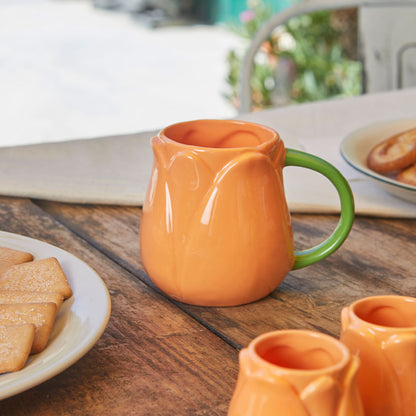 Orange Tulip mug on a wooden table with biscuits and more mugs