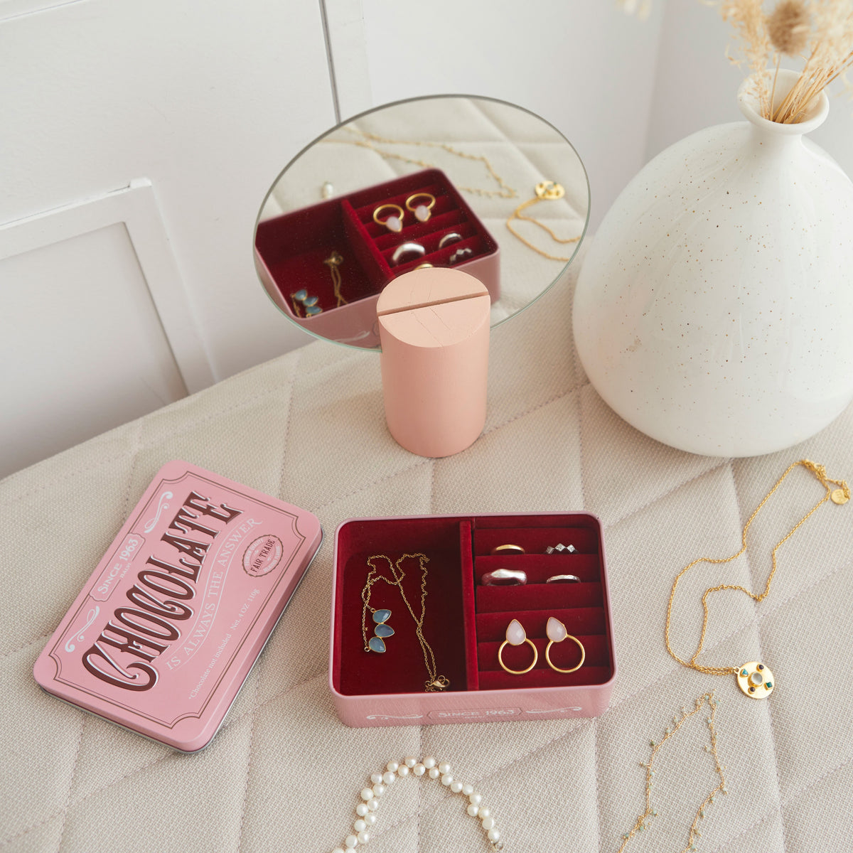 Portagioie Chocolate: la scatola rosa aperta con anelli sul tavolo tra specchio e vaso.
