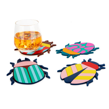 Beetle coasters placed under a whisky glass, among leaves on a white background.