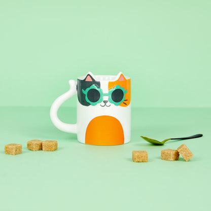 Tazza Cool Cat Calico su sfondo verde, con zollette di zucchero e un cucchiaino