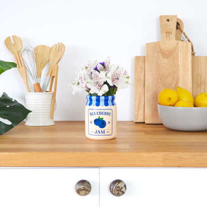 Jam vase, blueberry version with white flowers, on a worktop between chopping boards and lemons