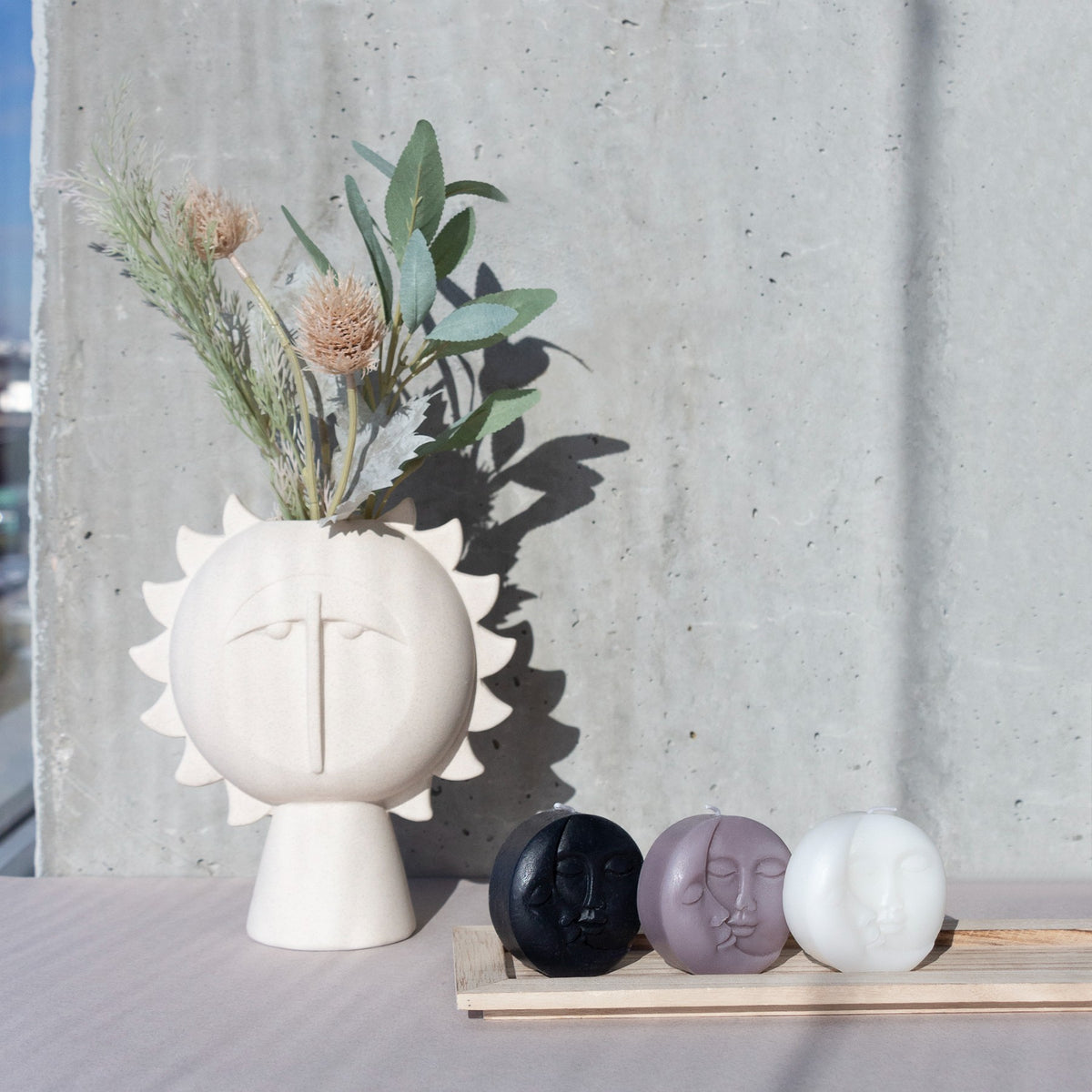Sun-face vase with dried branches, next to three small faces in black, mauve and white