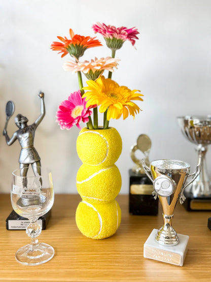 Ace Tennis Ball vase on a shelf, next to a trophy and a small tennis-player figurine.