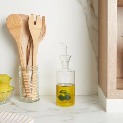 Olive oil cruet on a marble counter, next to a jar of wooden utensils and lemons