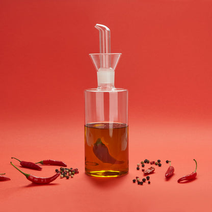 Oliera Chilli: la bottiglia di vetro con il peperoncino dentro, su sfondo rosso con peperoncini.