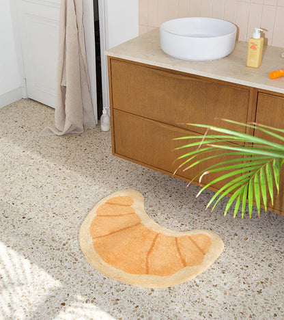 Croissant rug in honey tone in front of a white curtain near a plant