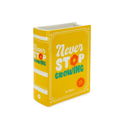 Yellow Book vase empty, with "never stop growing" printed on the cover, white background