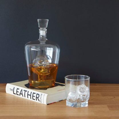 Poison Bottle: the whisky-filled decanter resting on a book, on a wooden table.