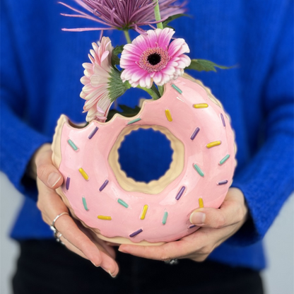 Doughnut vase in pink with flowers, held in front of the face by someone in a blue jumper.