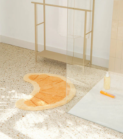 The croissant rug placed on the bathroom floor near a shower