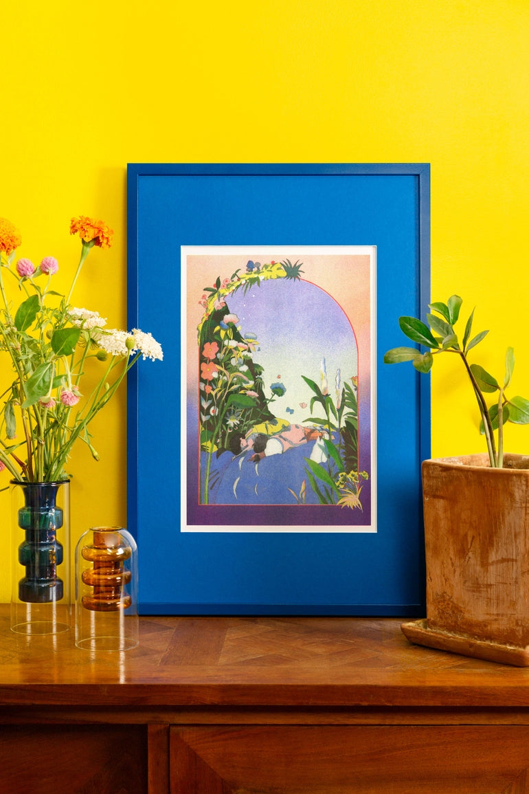Poster Sogno Totoro in cornice blu, appoggiato su una madia di legno tra vasi e piante