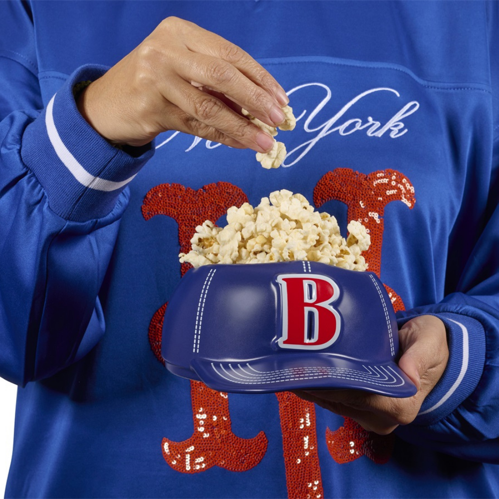 Baseball Cap bowl vase, a hand picking popcorn while holding it in the lap.