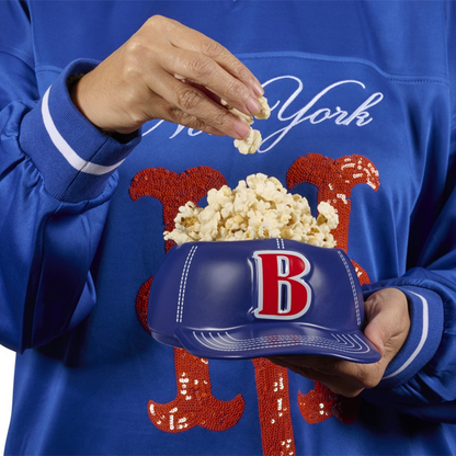 Baseball Cap bowl vase, a hand picking popcorn while holding it in the lap.