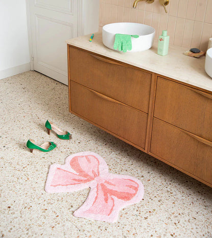 Soft bow rug in pink in front of a wooden vanity unit, green shoes nearby