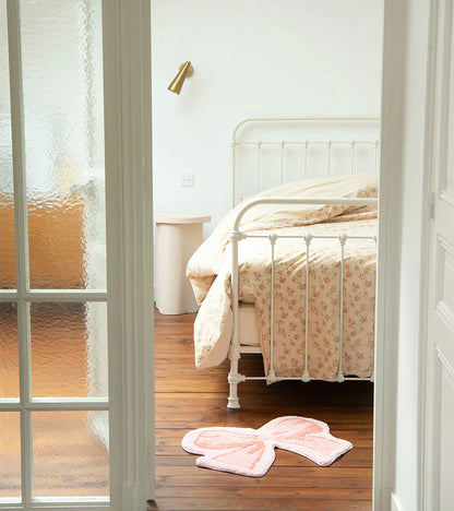 Soft bow rug in pink on a wooden floor beside a white bed