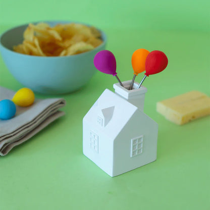 House Balloon snack forks holder on a green background, next to a bowl of crisps and cheese.