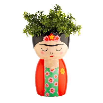 Vaso Frida a forma di volto con fiori tra i capelli, riempito da una pianta verde.