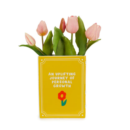 Yellow Book vase with "an uplifting journey of personal growth" printed and pink tulips
