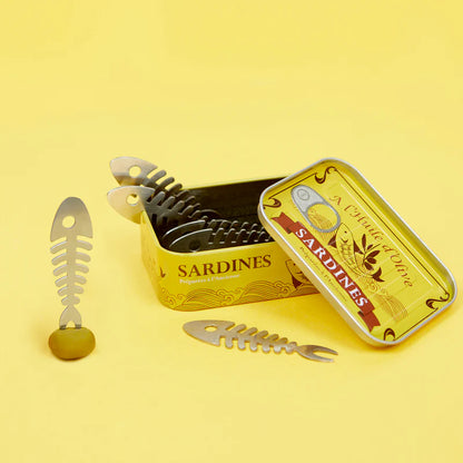 Fish-bone shaped cocktail forks with the sardine-tin style box, on a yellow background.